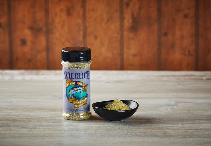 Wildlife Seasonings Swordfish Lemon Pepper 4.25 oz. bottle beside a small bowl of the seasoning on a rustic wood table