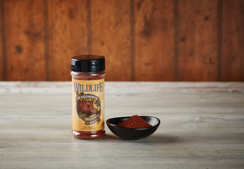 Wildlife Seasonings Wild Boar Rib Rub 5.0 oz. bottle beside a small bowl of the rub on a rustic wood table