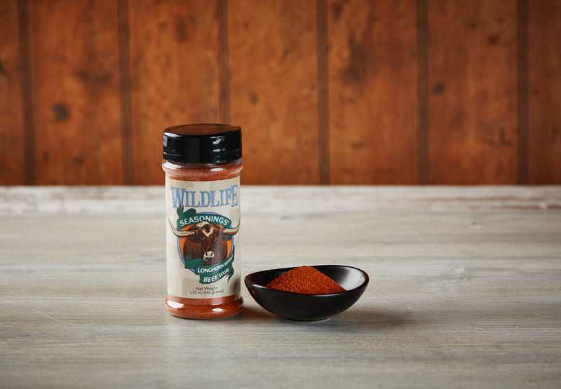 Wildlife Seasonings Longhorn Brisket Beef Rub 5.75 oz. bottle beside a small bowl of the rub on a rustic wood table
