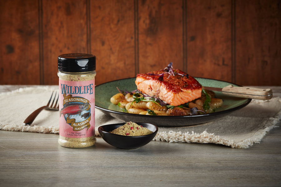 Wildlife Seasonings Alaskan Salmon Seasoning bottle and a bowl of the blend beside a plated salmon fillet with roasted potatoes