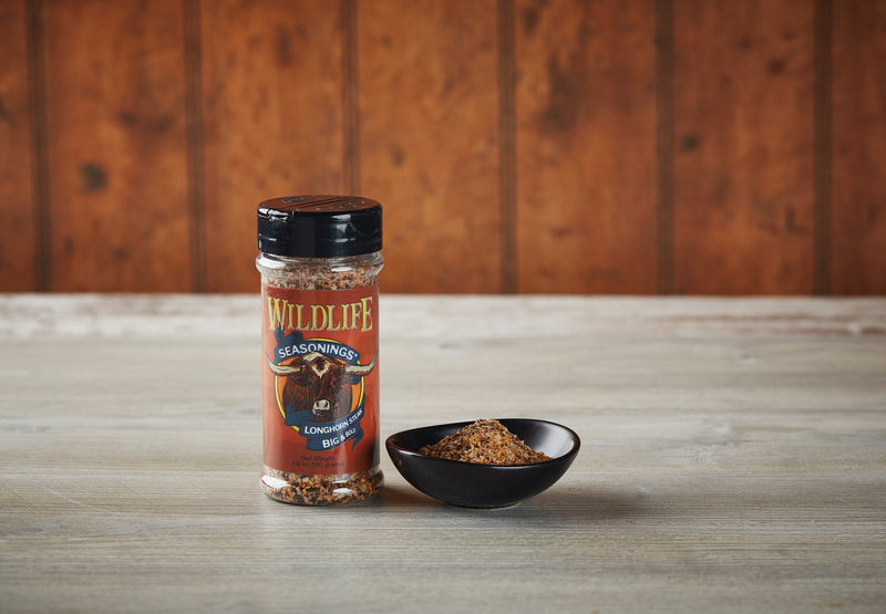 Wildlife Seasonings Longhorn Steak Big & Bold 6.0 oz. bottle beside a small bowl of the seasoning on a rustic wood table