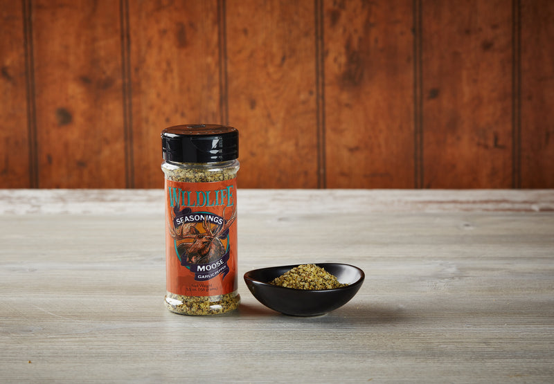 Wildlife Seasonings Moose Garlic Pepper 5.5 oz. bottle beside a small bowl of the seasoning on a rustic wood table