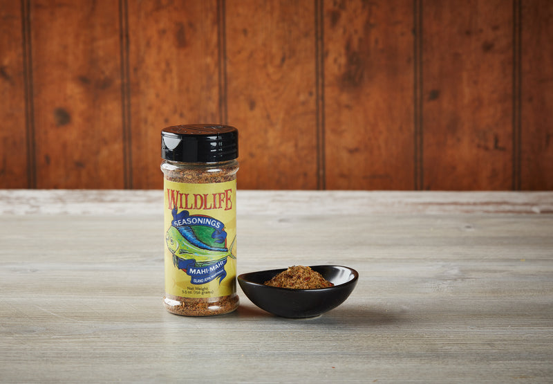 Wildlife Seasonings Mahi-Mahi Island Jerk Rub & Marinade 5.5 oz. bottle beside a small bowl of the seasoning on a rustic wood table