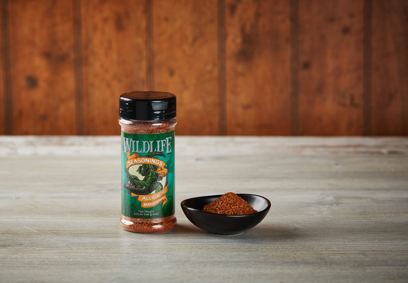 Wildlife Seasonings Alligator Bayou Cajun 5.25 oz. bottle beside a small bowl of the seasoning on a rustic wood table