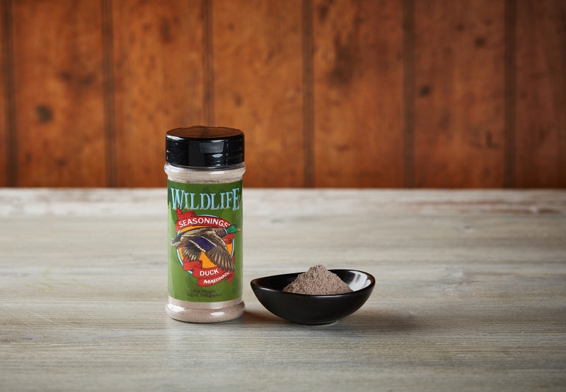 Wildlife Seasonings Duck Marinade 4.5 oz. bottle beside a small bowl of the wine-based marinade powder on a rustic wood table