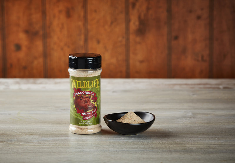 Wildlife Seasonings Smoky Boar Applewood Smoke Rub 6.75 oz. bottle beside a small bowl of the rub on a rustic wood table