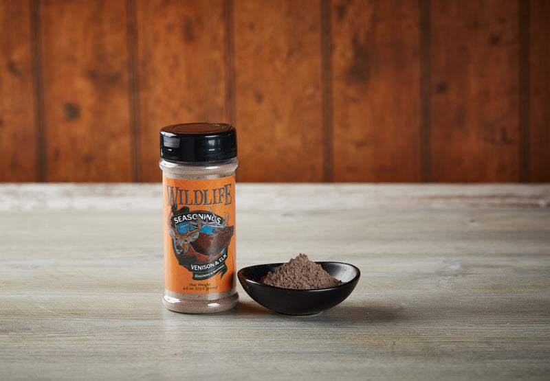 Wildlife Seasonings Venison & Elk Seasoning and Marinade 4.0 oz. bottle beside a small bowl of the seasoning on a rustic wood table